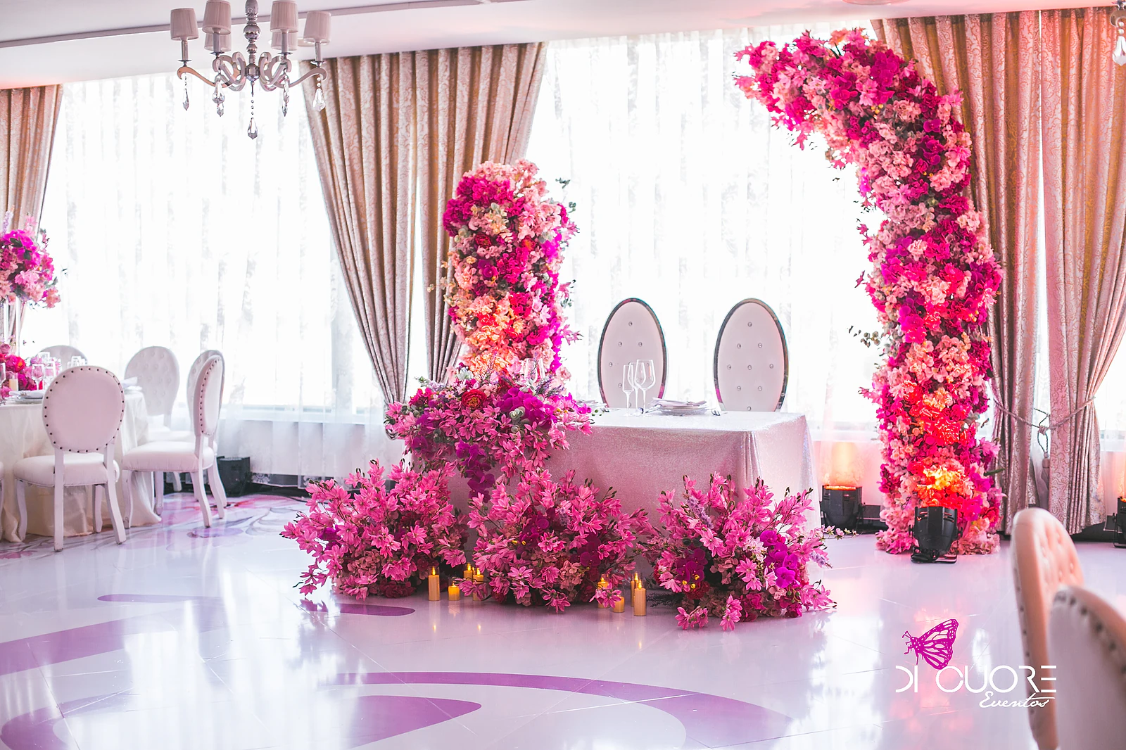 Mesa de honra com arcos de flores cor-de-rosa e magenta num salão de hotel