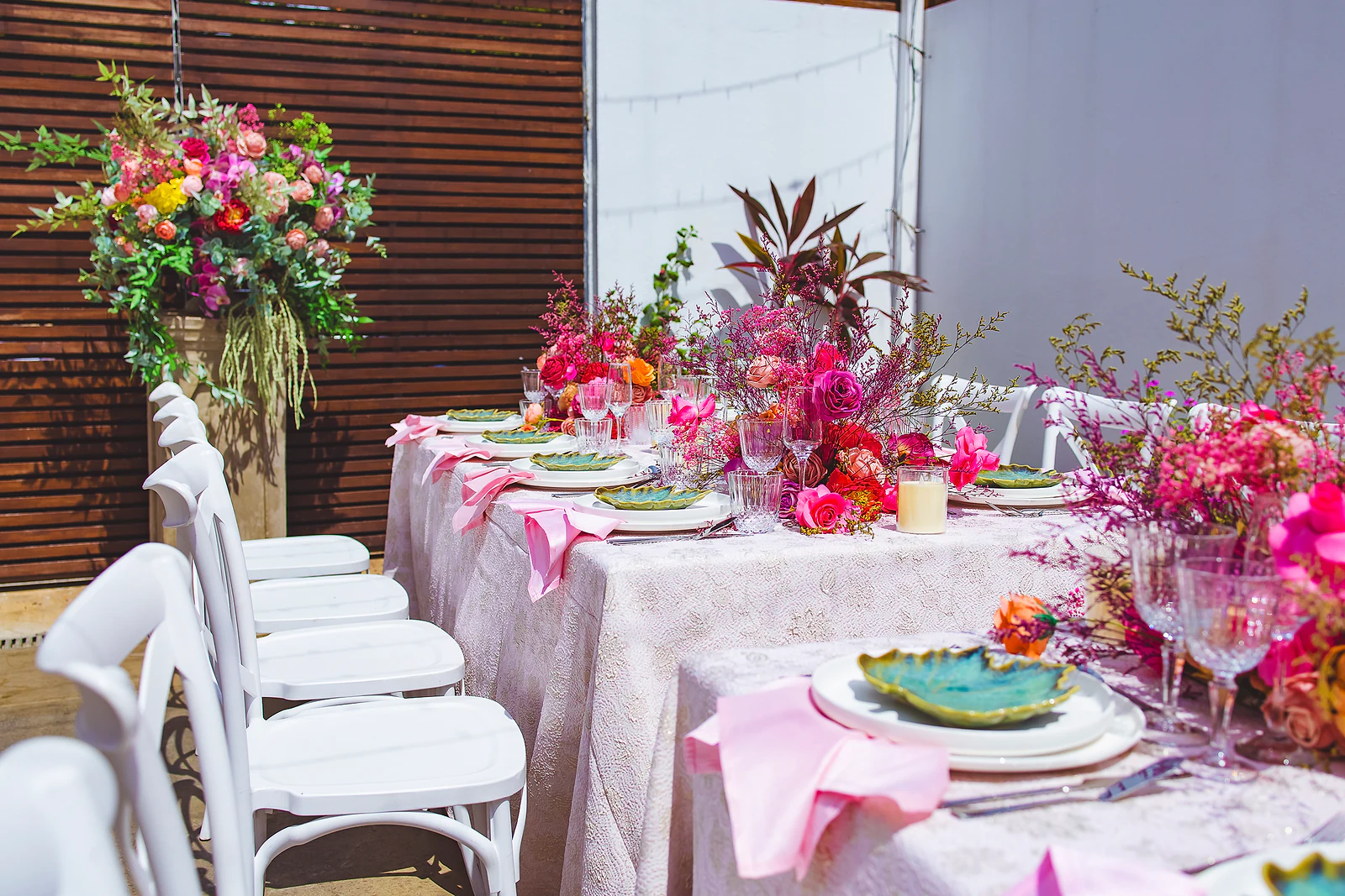 Mesa posta com toalha texturada, cadeiras brancas e arranjos magenta