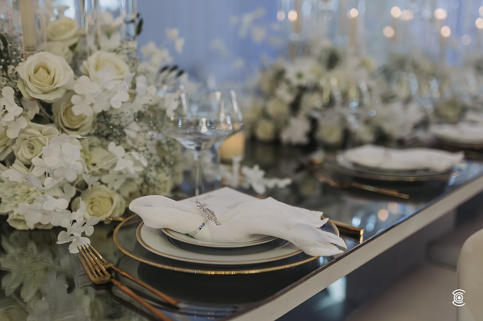 Pormenor da mesa com rosas brancas, pratos dourados e copos de cristal